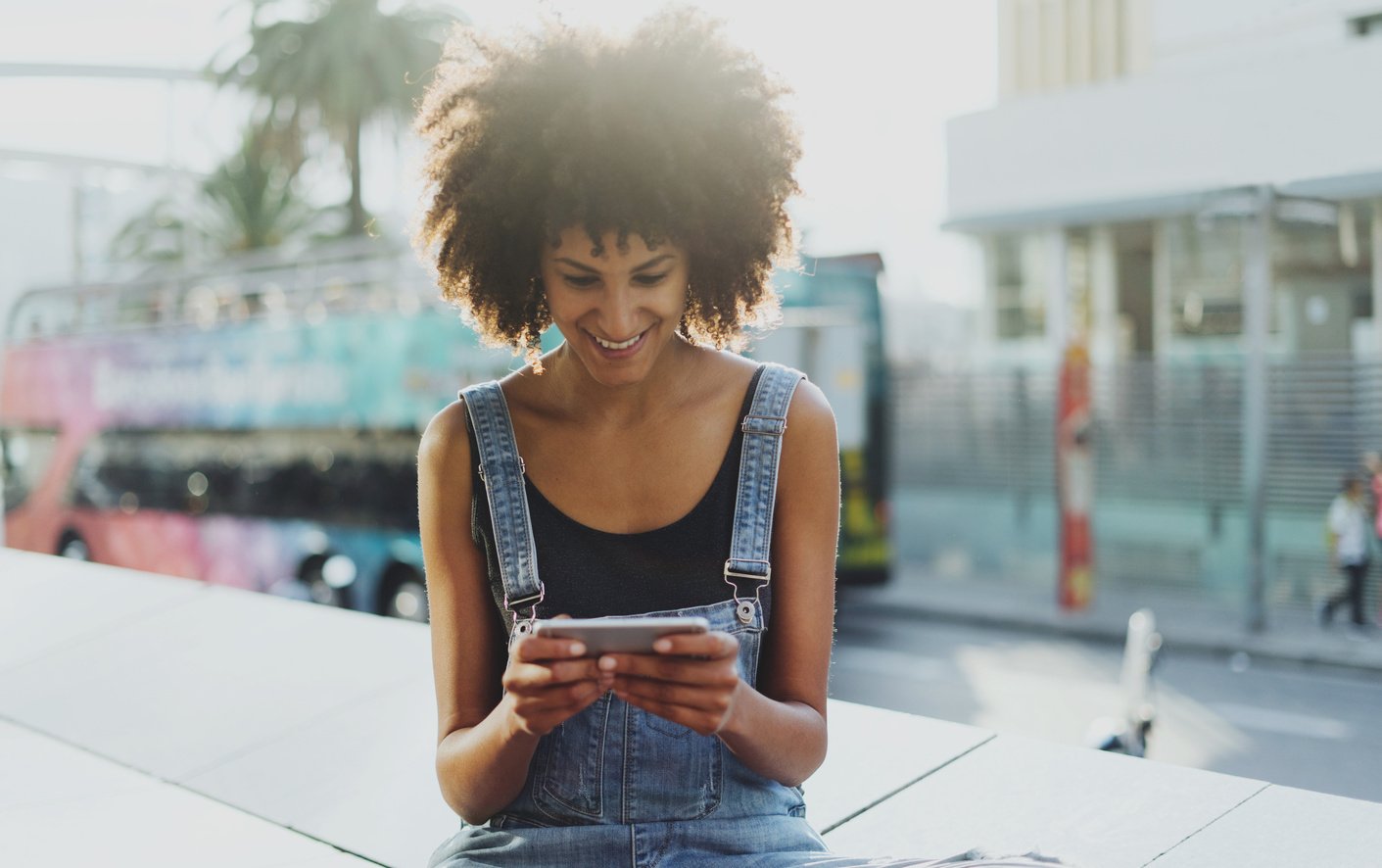 a beautiful dark-skinned girl reads a newsletter in social networks using a mobile phone and a public WiFi while resting outside.Young female student chatting with classmates discussing upcoming exams